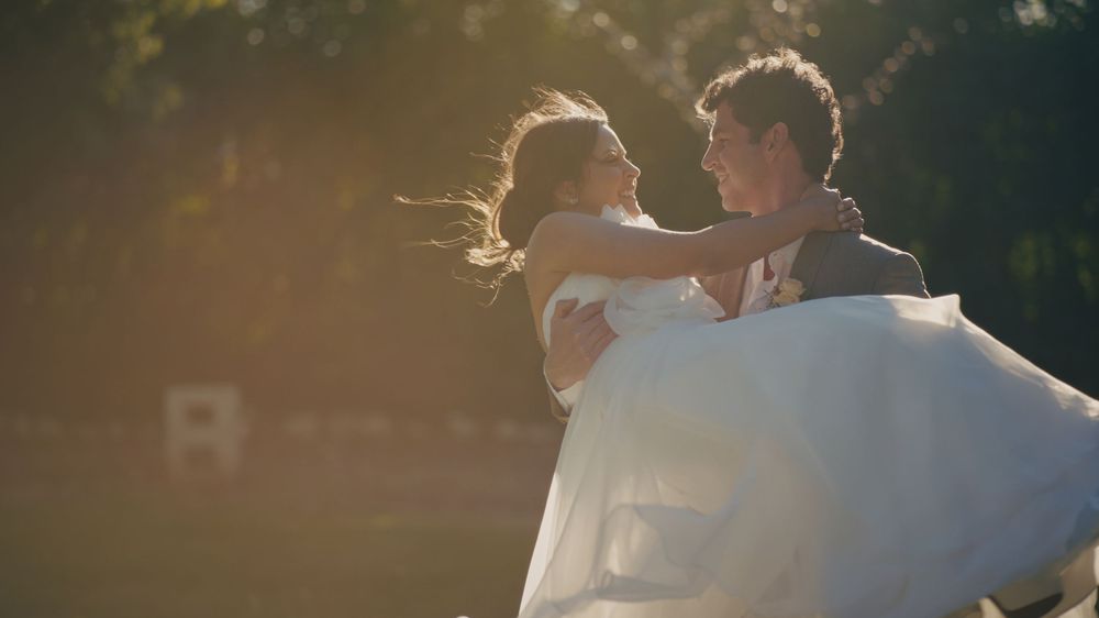 A couple shares a romantic embrace while dancing in golden sunlight, with the bride wearing a flowing white gown.