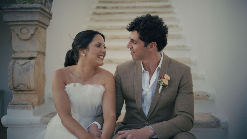 A couple in brown and white wedding attire share intimate moments on grand stone steps at dusk.