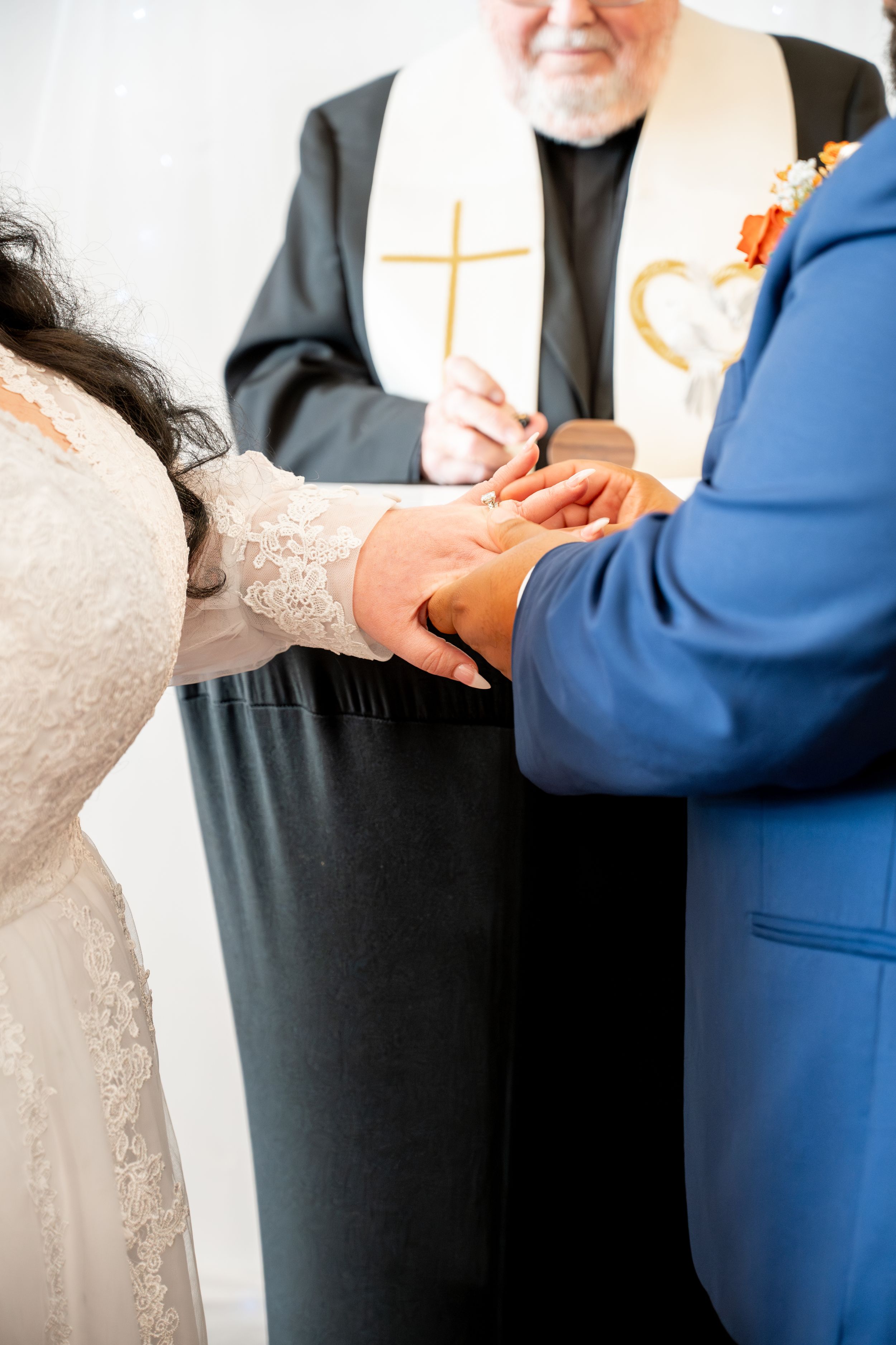Close-up of wedding ceremony details with hands and white lace dress visible.
