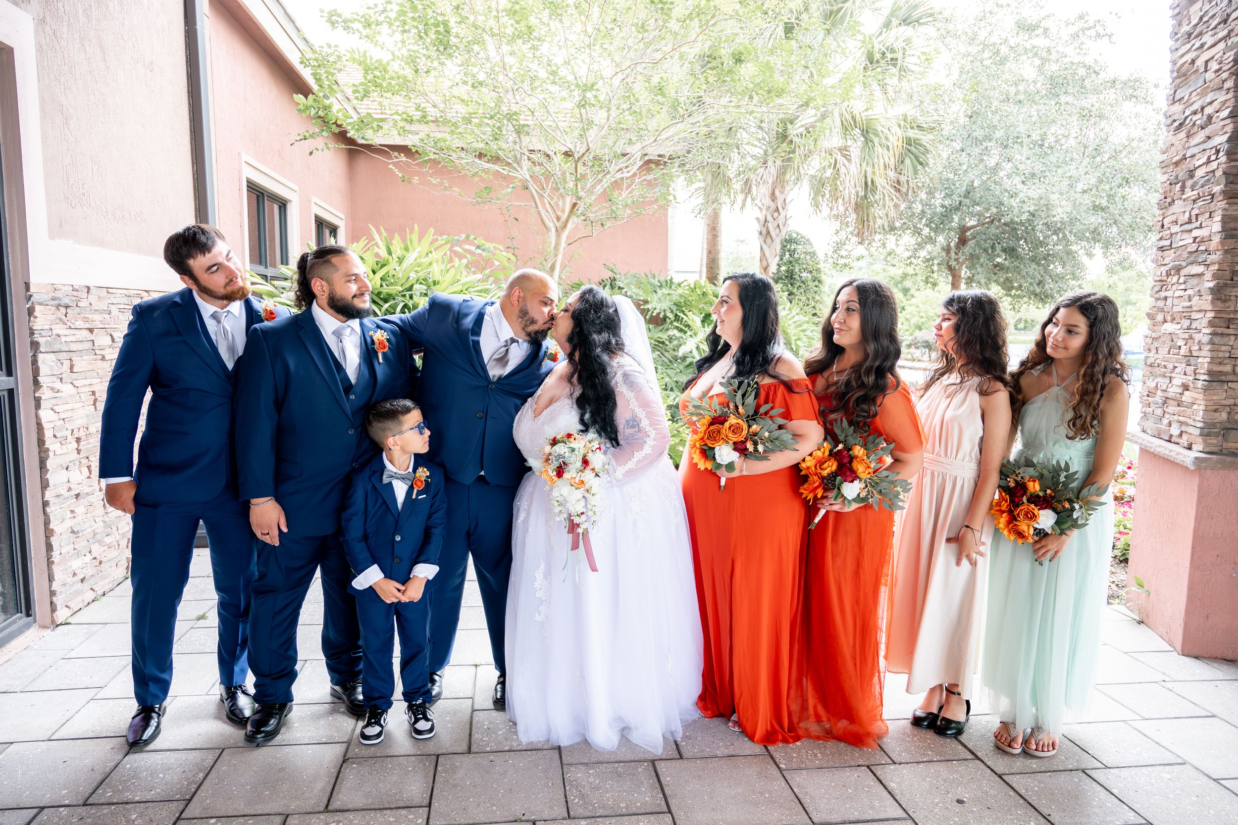 Wedding party poses together under covered walkway wearing navy suits and colorful dresses.