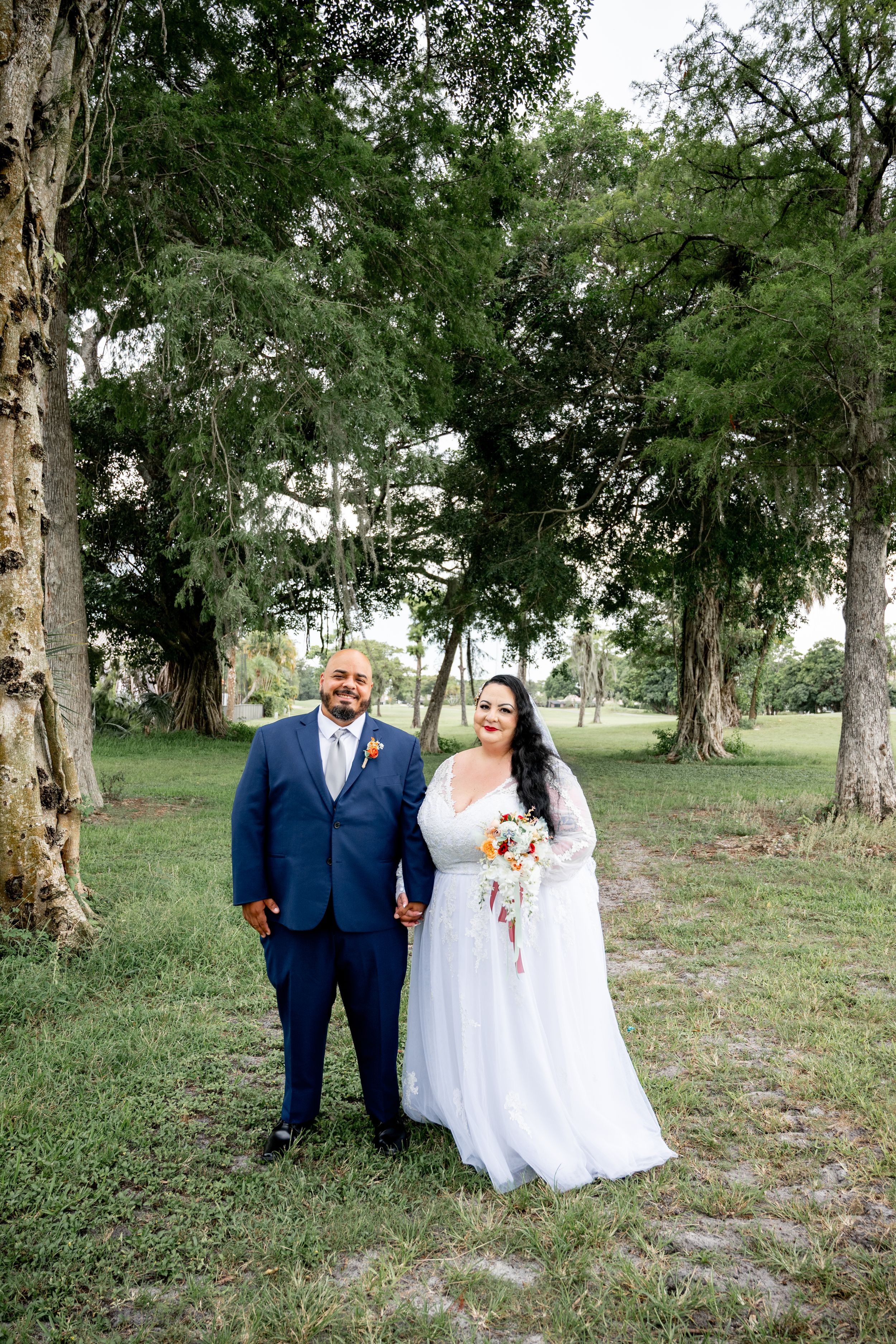 Wedding portraits taken in a serene park setting with mature trees.