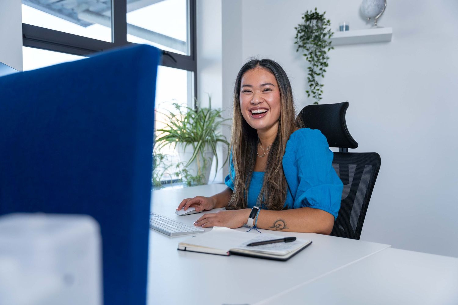 Staff headshot photography with a business in Southampton. Woman sits at her desk in a modern office smiling to camera.