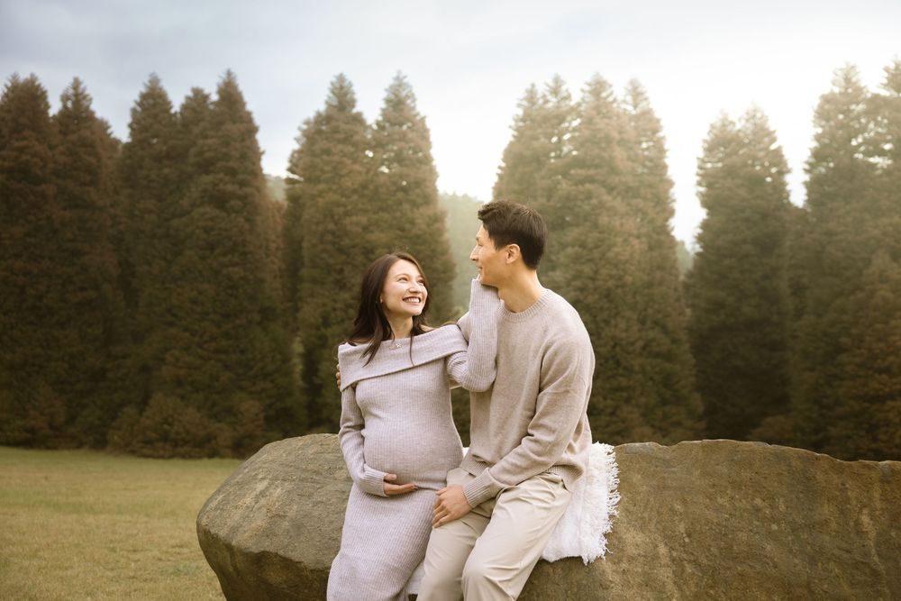 A couple poses together in nature during a romantic photo session at sunset in front of tall evergreen trees.