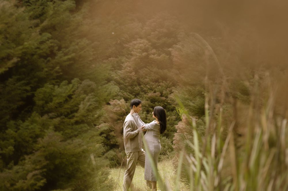 A couple embraces in a romantic outdoor setting with sunlit mountains and greenery in the background.
