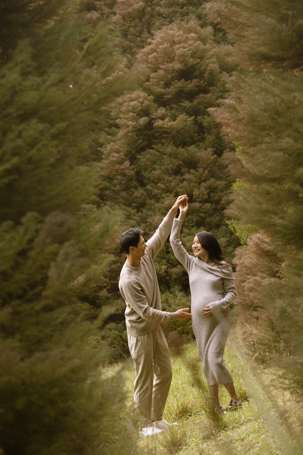 Couple dancing together on a grassy hillside against a backdrop of autumn trees in warm muted tones.