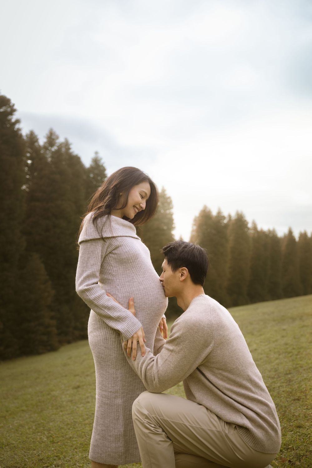 Intimate maternity moment captured outdoors with pine trees in the background.