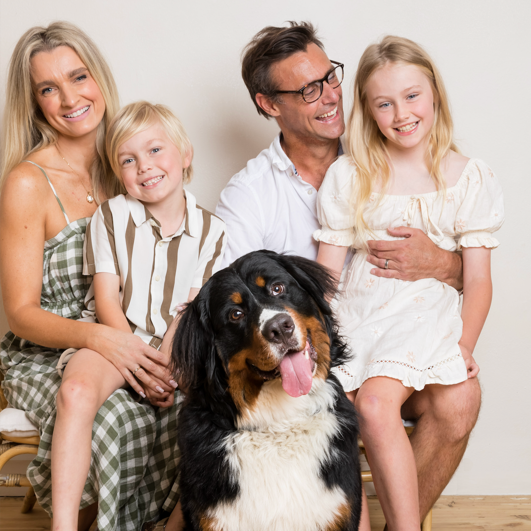 Studio portrait of a family with their Bernese Mountain Dog sitting together on a bench.