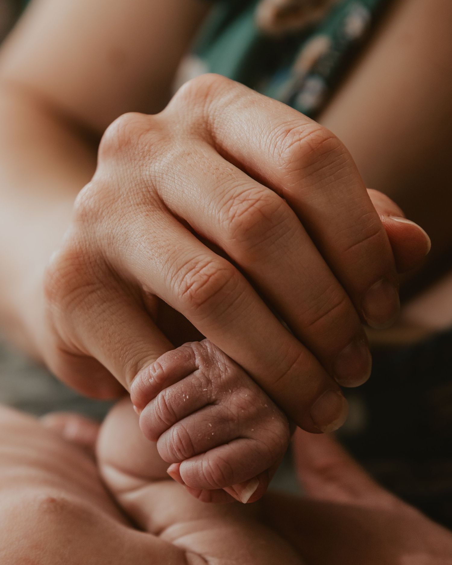 Sleeping baby with pacifier being gently held by adult hands in warm ambient lighting.