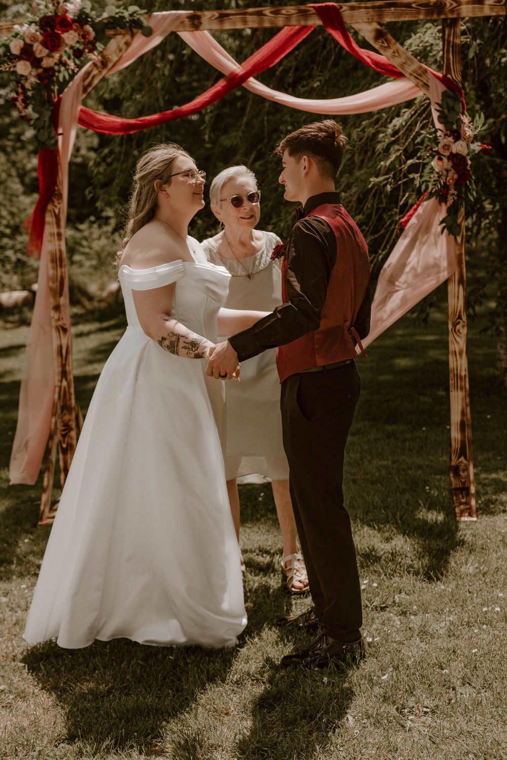 Bride and groom holding hands at outdoor wedding ceremony with officiant present.