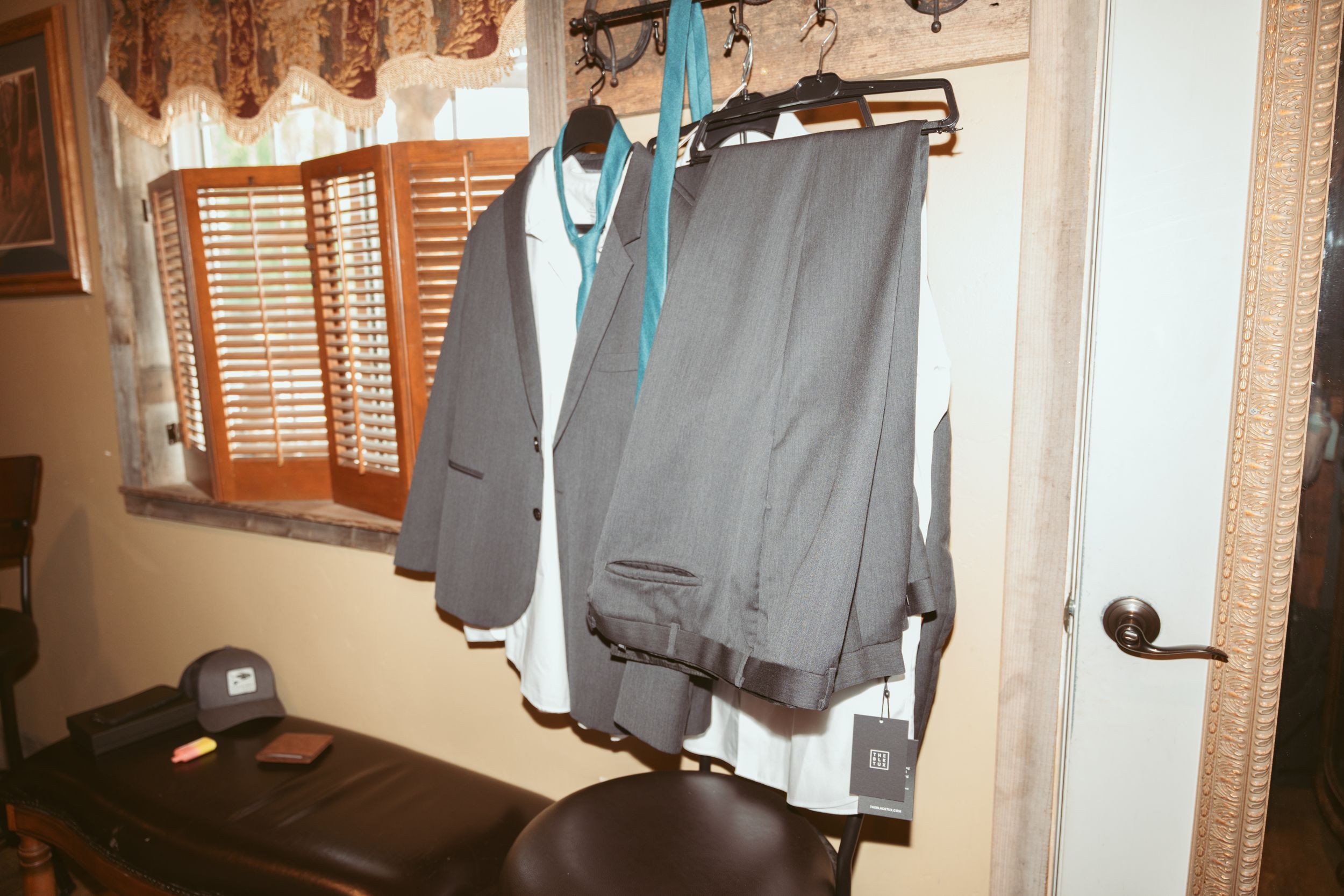 An array of clothes hanging on a wall-mounted rack against a cream-colored wall near wooden window shutters.