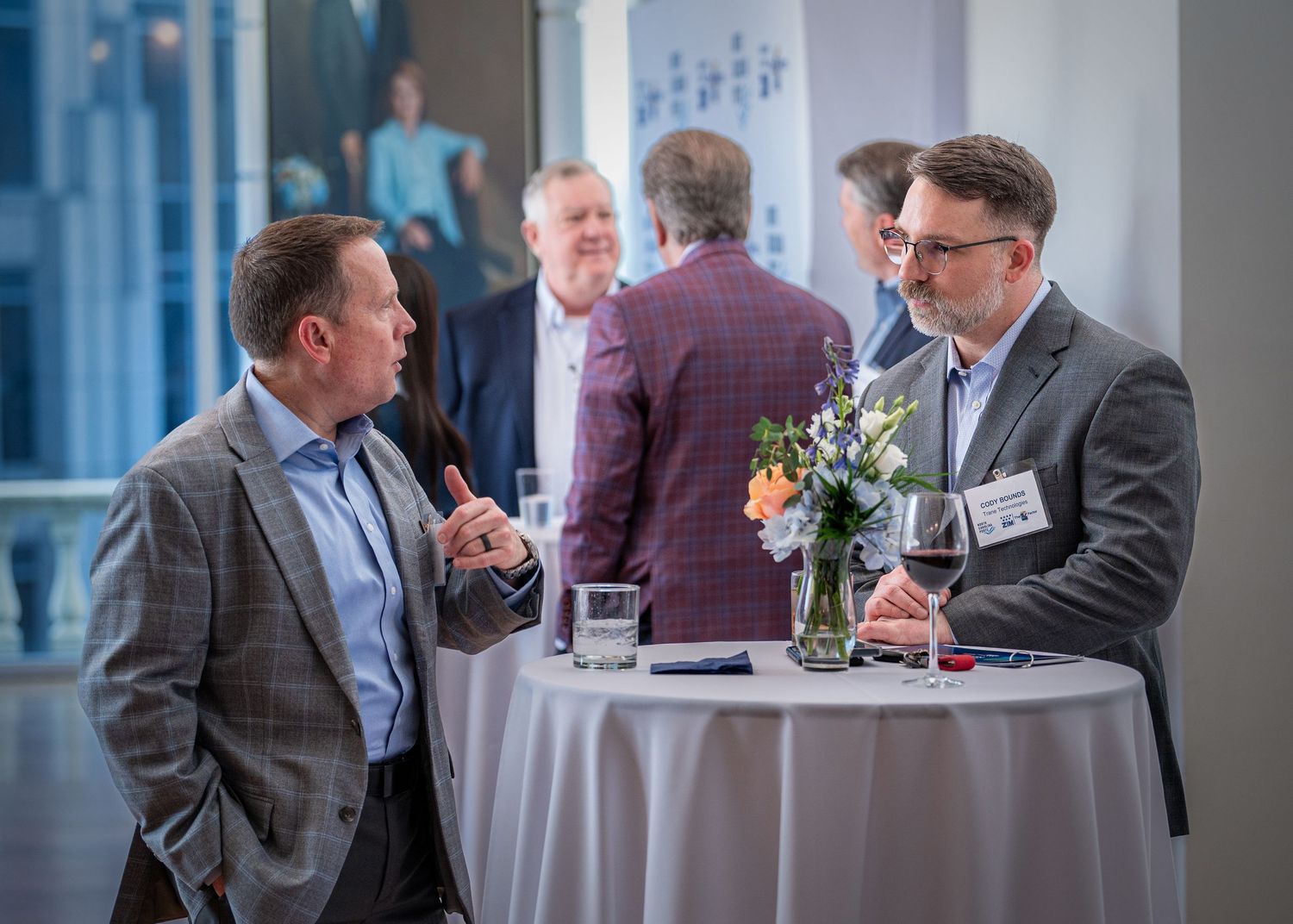 Two professionals having animated discussion at cocktail table with floral centerpiece.