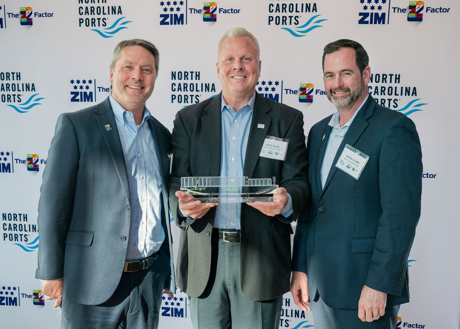 Three professionals pose with award at corporate event with branded backdrop.