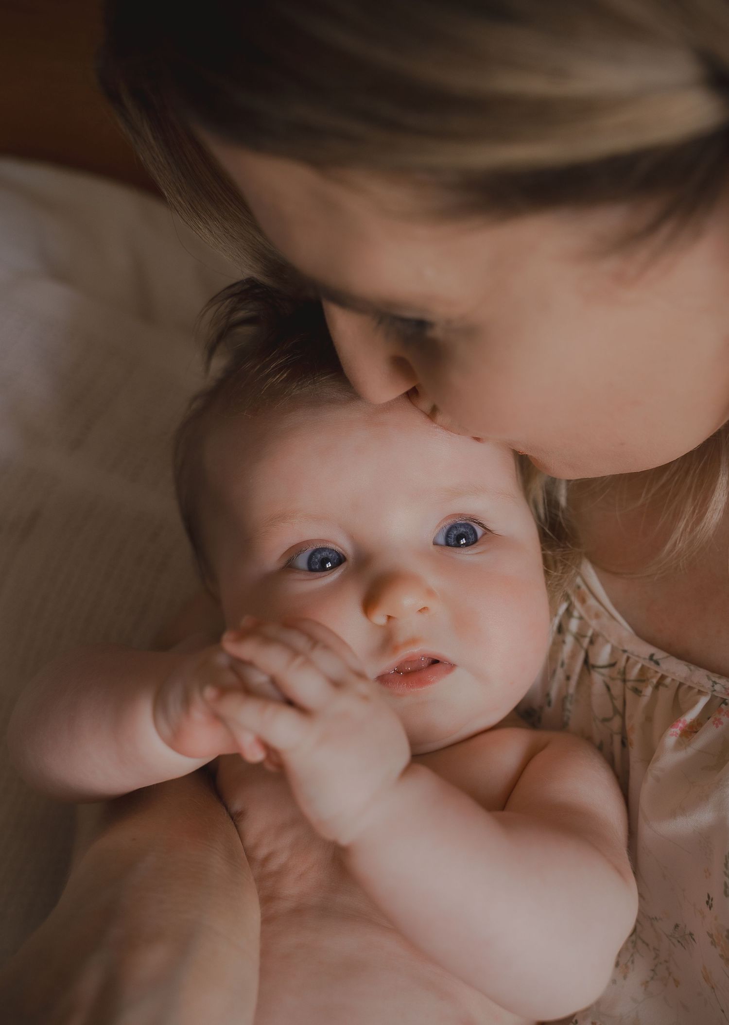 A close-up of a baby held in their mother’s arms, gazing up with curiosity and wonder during an in-home newborn session in Leicestershire.