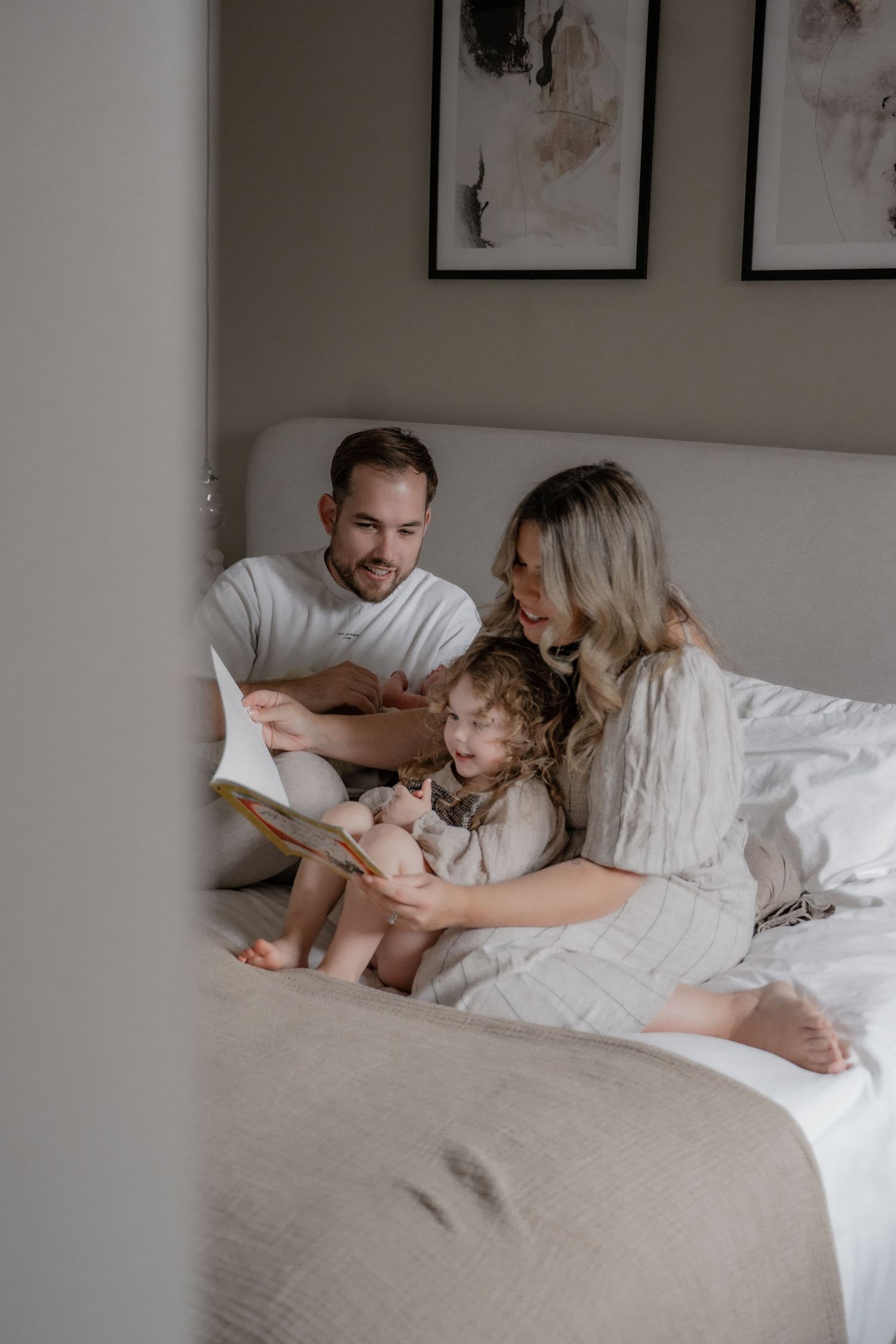 A family of four reading together on the bed during a relaxed in-home photo shoot in Leicestershire, surrounded by soft natural light and co