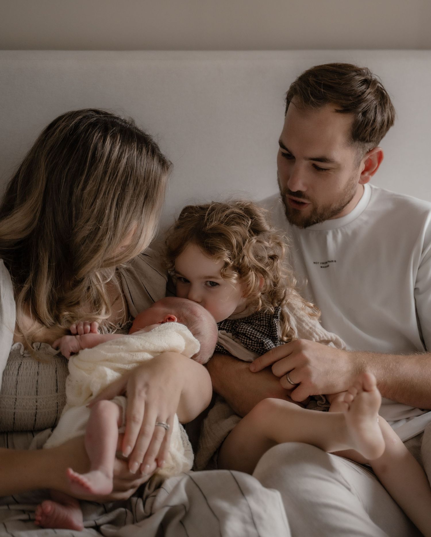 A family cuddled close on the bed — the older sibling kissing the baby while both parents look on lovingly — during an honest and emotional