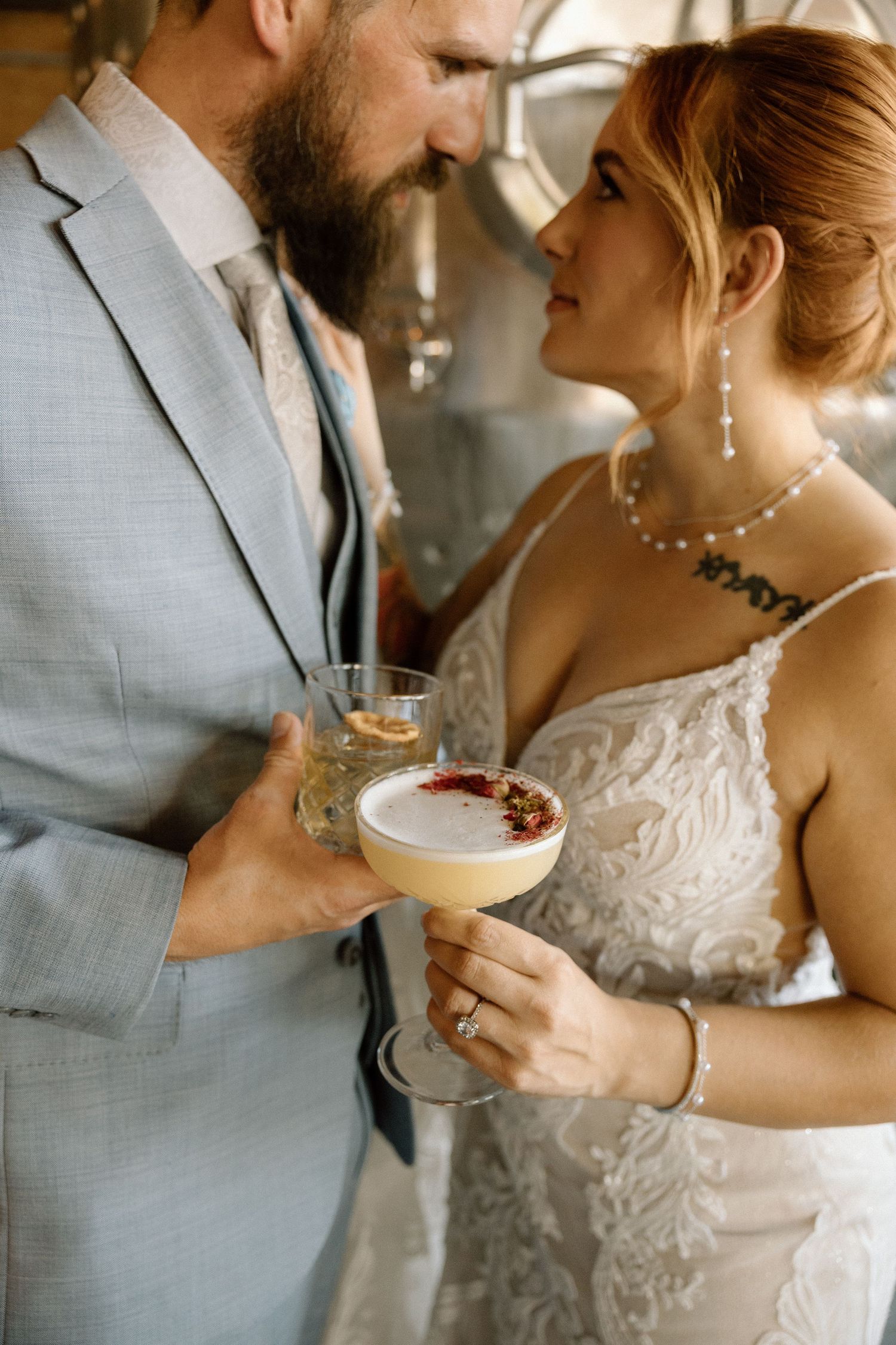 A couple shares cocktails during their wedding celebration in front of metallic tanks.