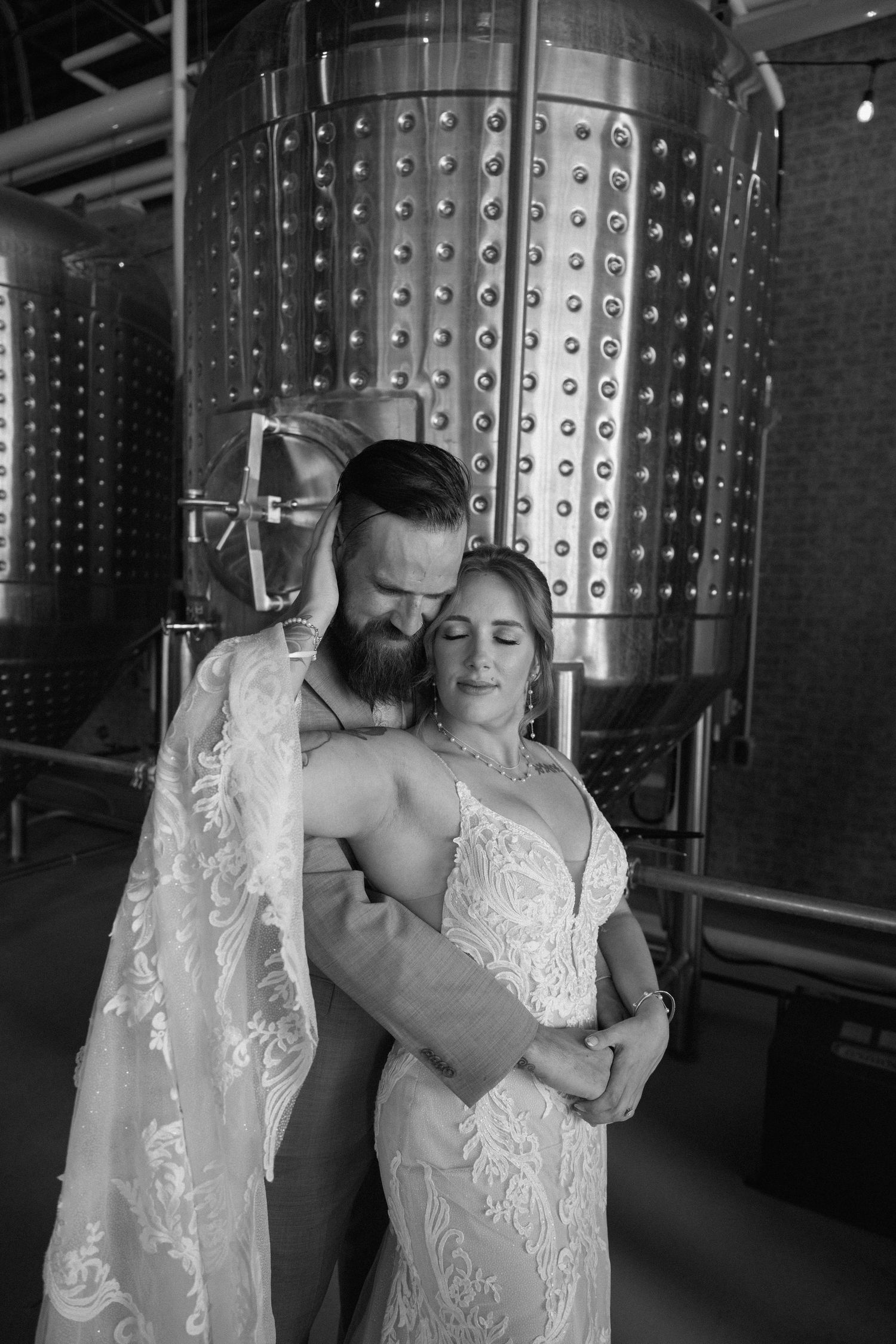 Couple dancing intimately in a wine cellar with stainless steel fermentation tanks.