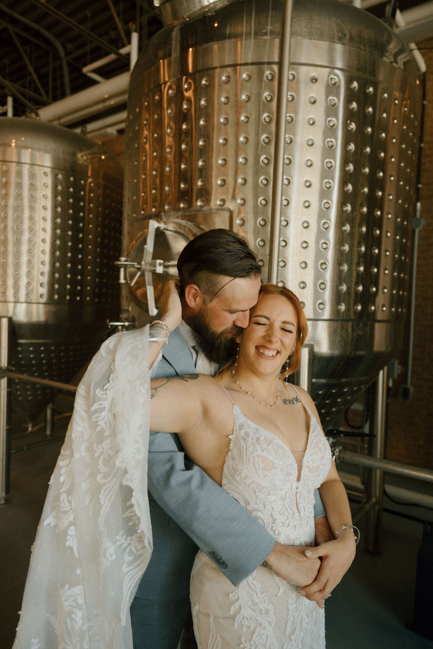Romantic couple embracing in a winery cellar with stainless steel fermentation tanks in the background.