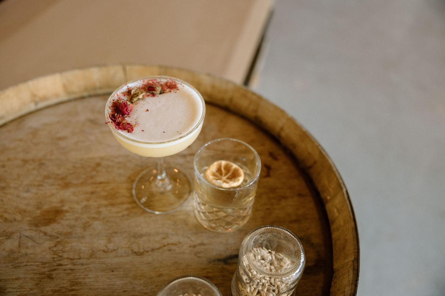 A glass filled with creamy layered cocktail garnished with red fruit sits on a rustic wooden surface.