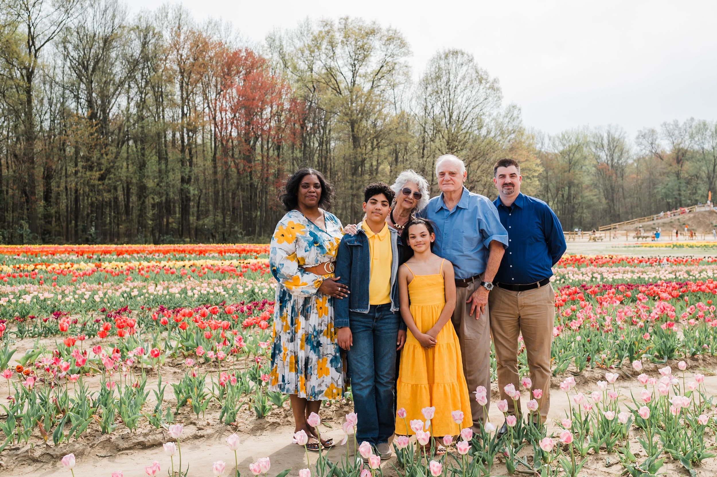 A group stands together in a colorful tulip field during spring with trees in the background.