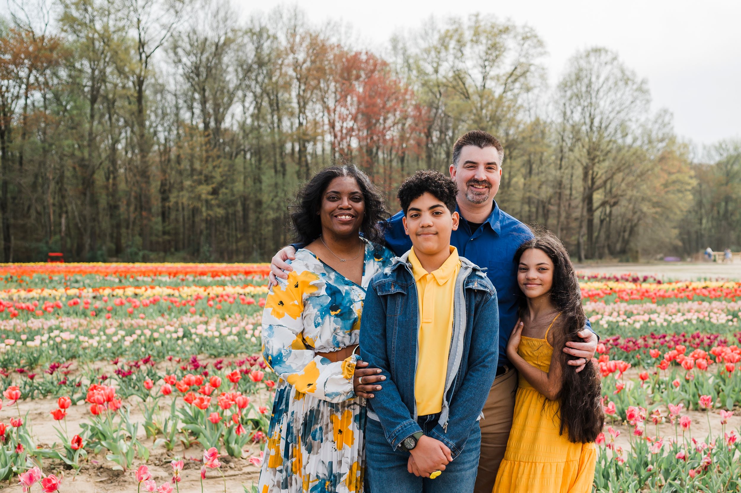 Four people standing together in a colorful tulip field during spring with trees in the background.