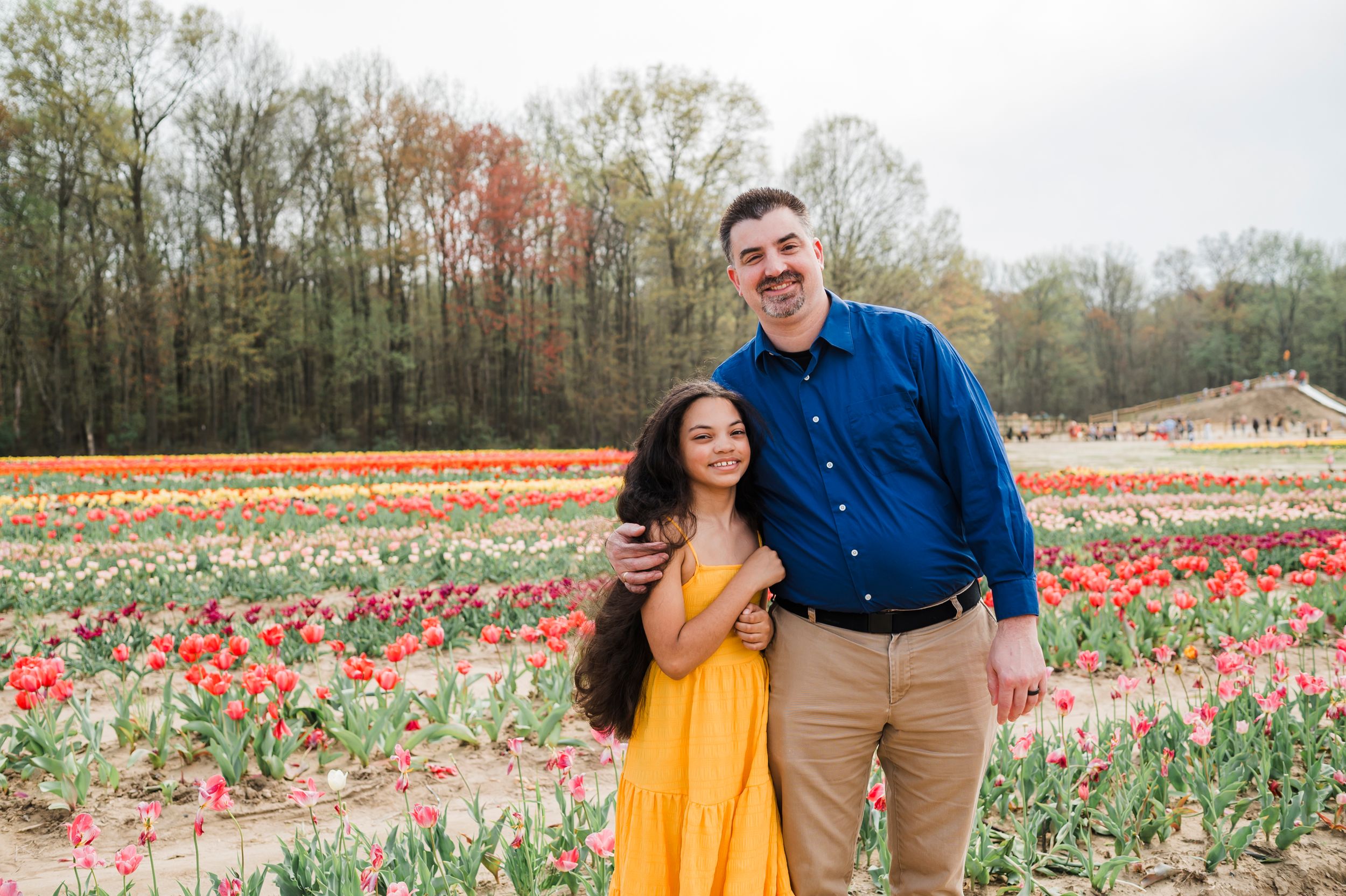 Two people pose together and laugh while standing among colorful blooming tulip fields on a spring day.