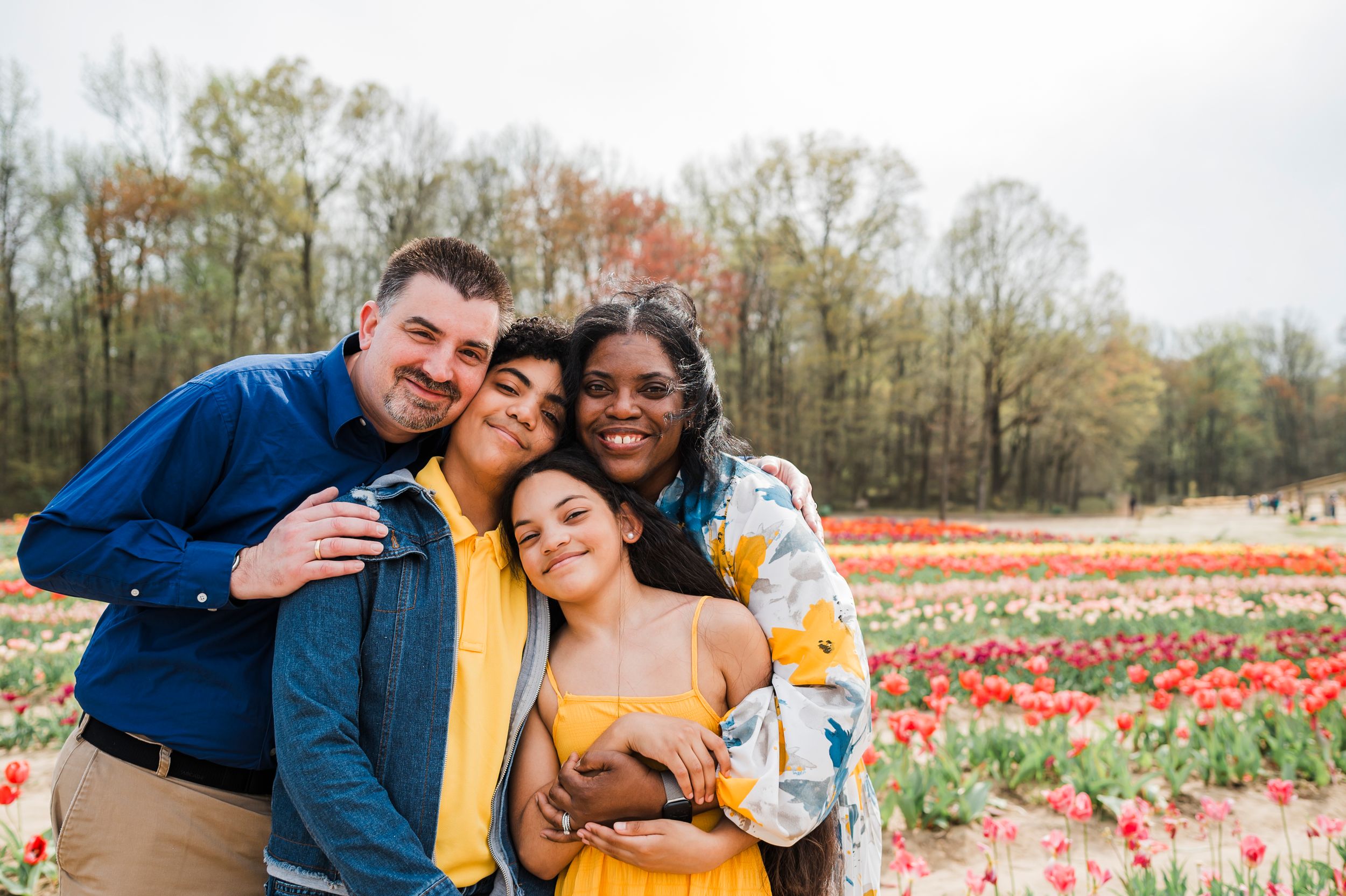 A happy group stands together smiling in front of colorful tulip fields on a spring day.