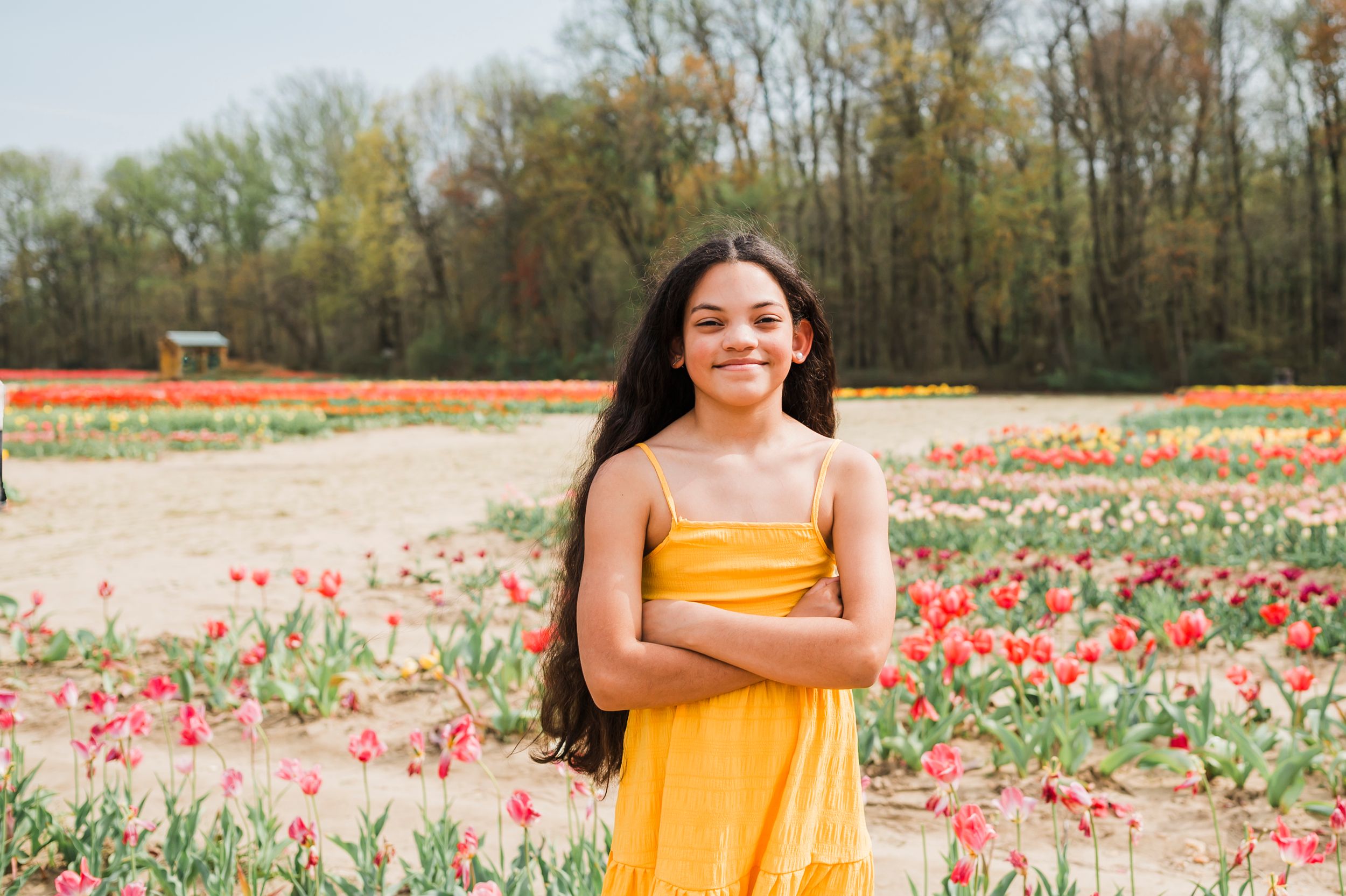 A person in a bright yellow dress poses in a colorful tulip field during spring bloom season.