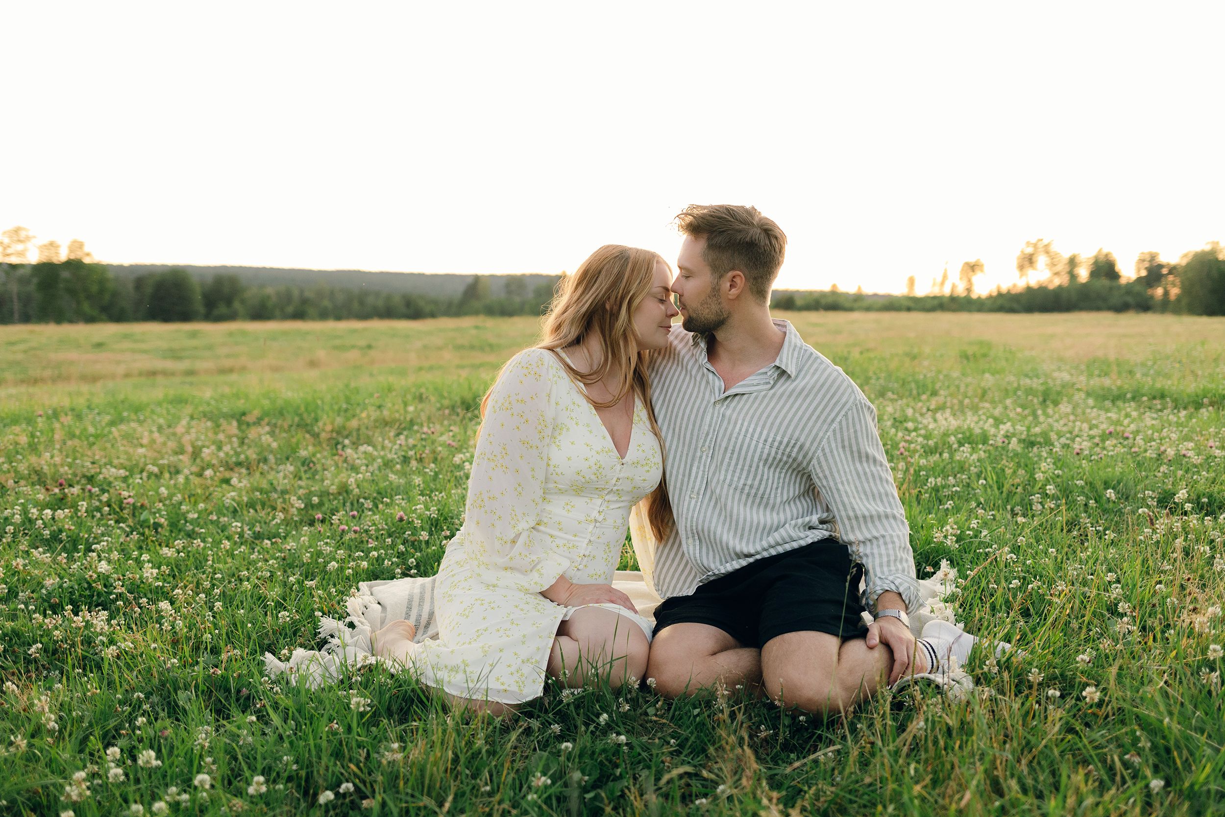 Paret Martina och Sebastian under en kärleksfotografering på äng i Borgvik, Karlstad. Fotograf Rebecca Nordin. Sittandes på filt.