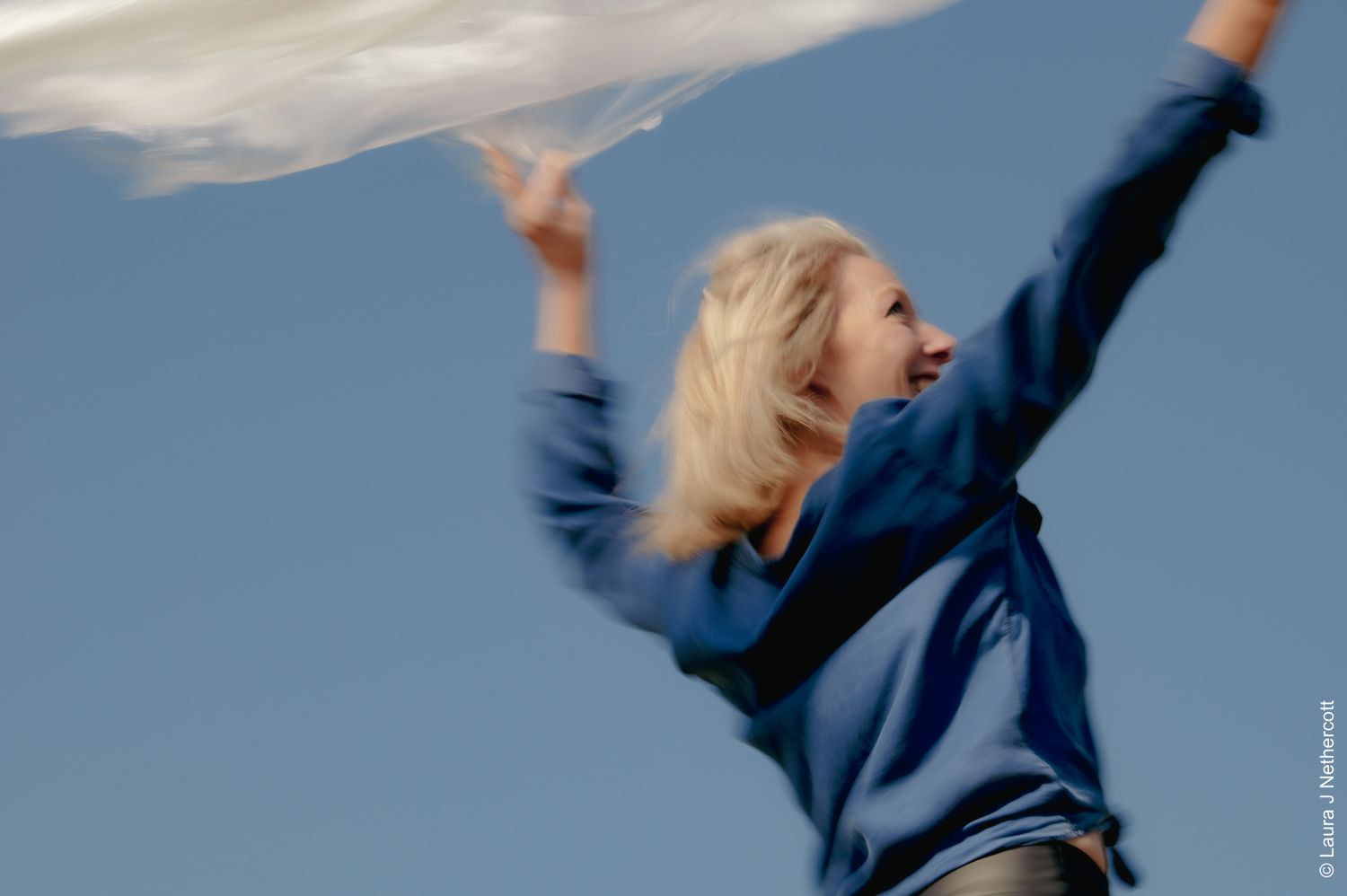 Dynamic motion blur photograph of person jumping against blue sky.