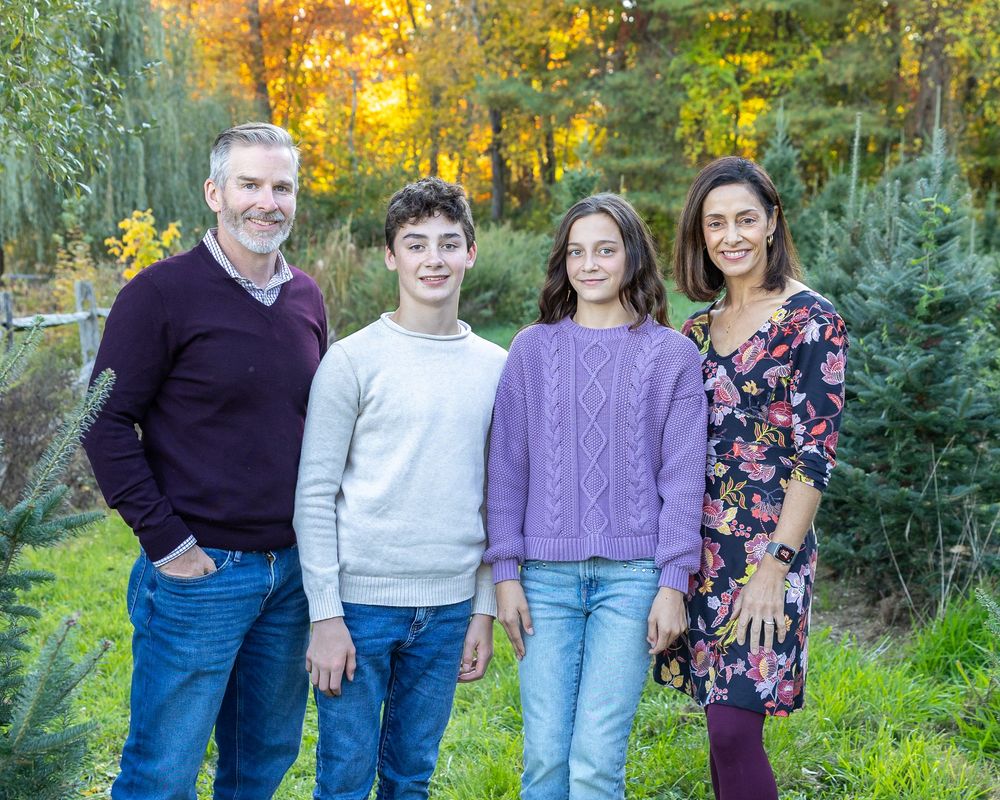 A family poses together in a field of Christmas trees at Mistletoe Christmas Tree Farm in Stow, MA by Lisa West Photography