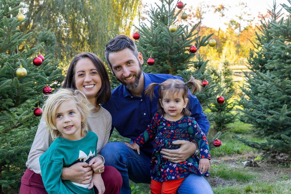 A family poses together in front of a decorated Christmas tree at Mistletoe Christmas Tree Farm in Stow, MA at holiday photo shoot.