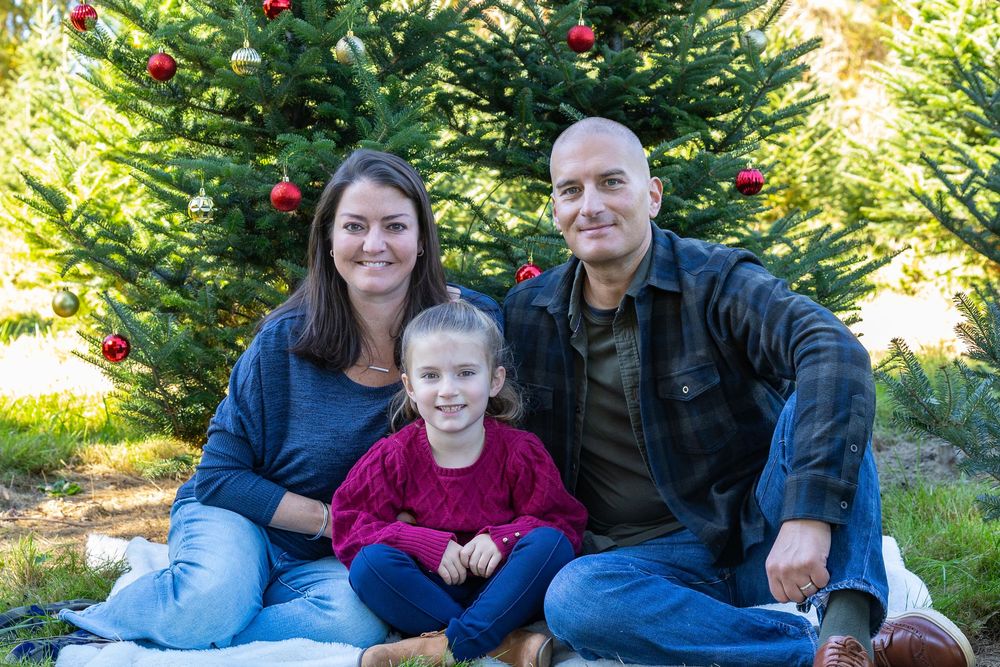 A family poses together in front of a decorated Christmas tree at Mistletoe Christmas Tree Farm in Stow, MA at holiday photo shoot.