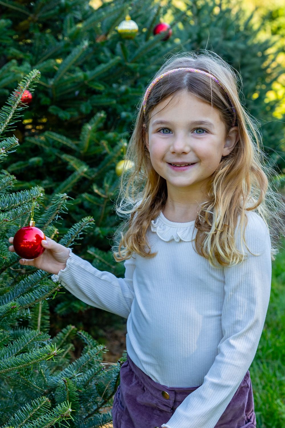 A girl decorates a christmas tree in a field at Mistletoe Christmas Tree Farm in Stow, MA at holiday photo shoot by Lisa West Photography.