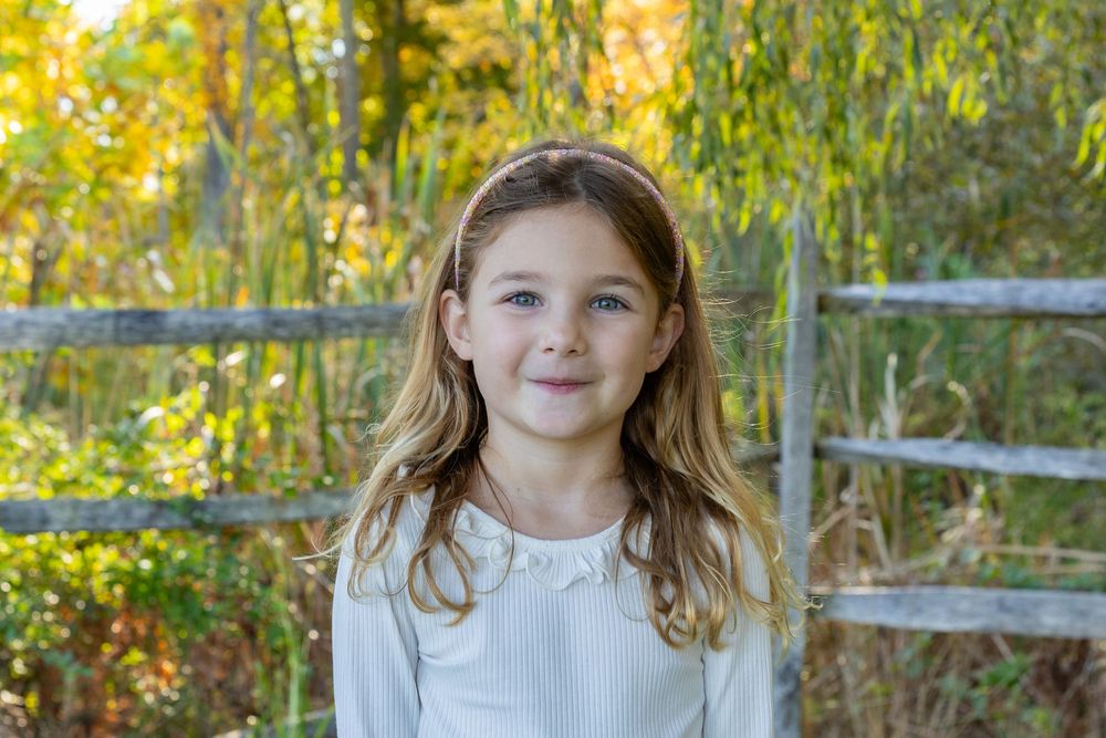 A girl poses on an autumn day with colorful fall foliage at Mistletoe Christmas Tree Farm in Stow, MA at holiday photo shoot by Lisa West
