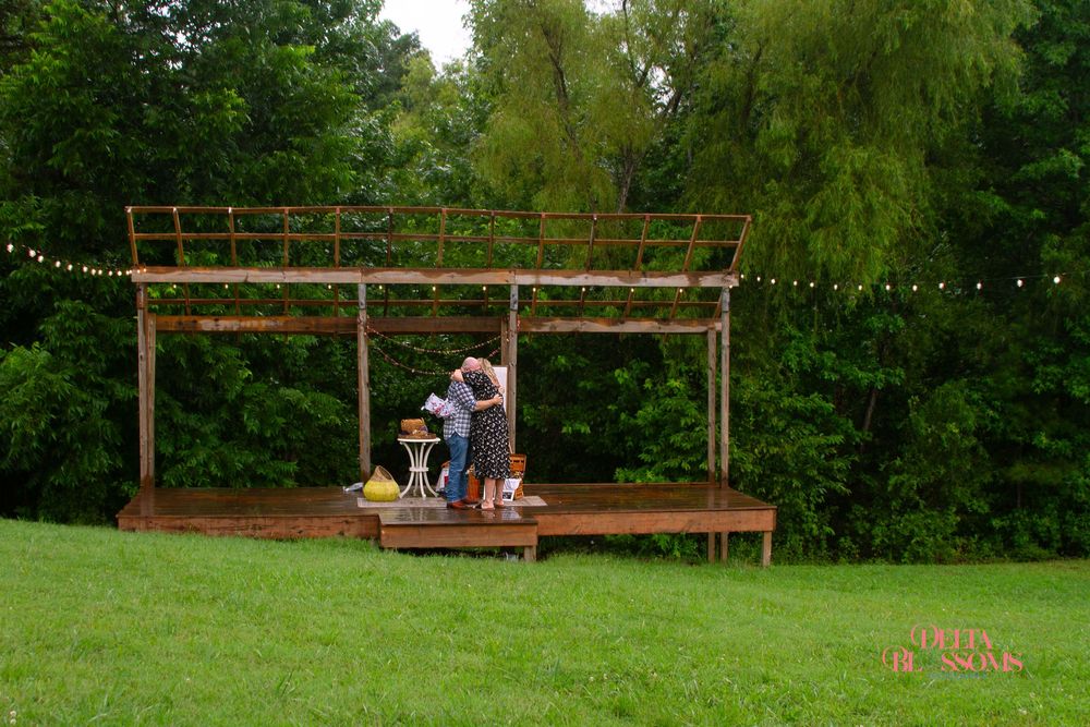 a newly engaged couple standing on a rustic stage with trees in the background
