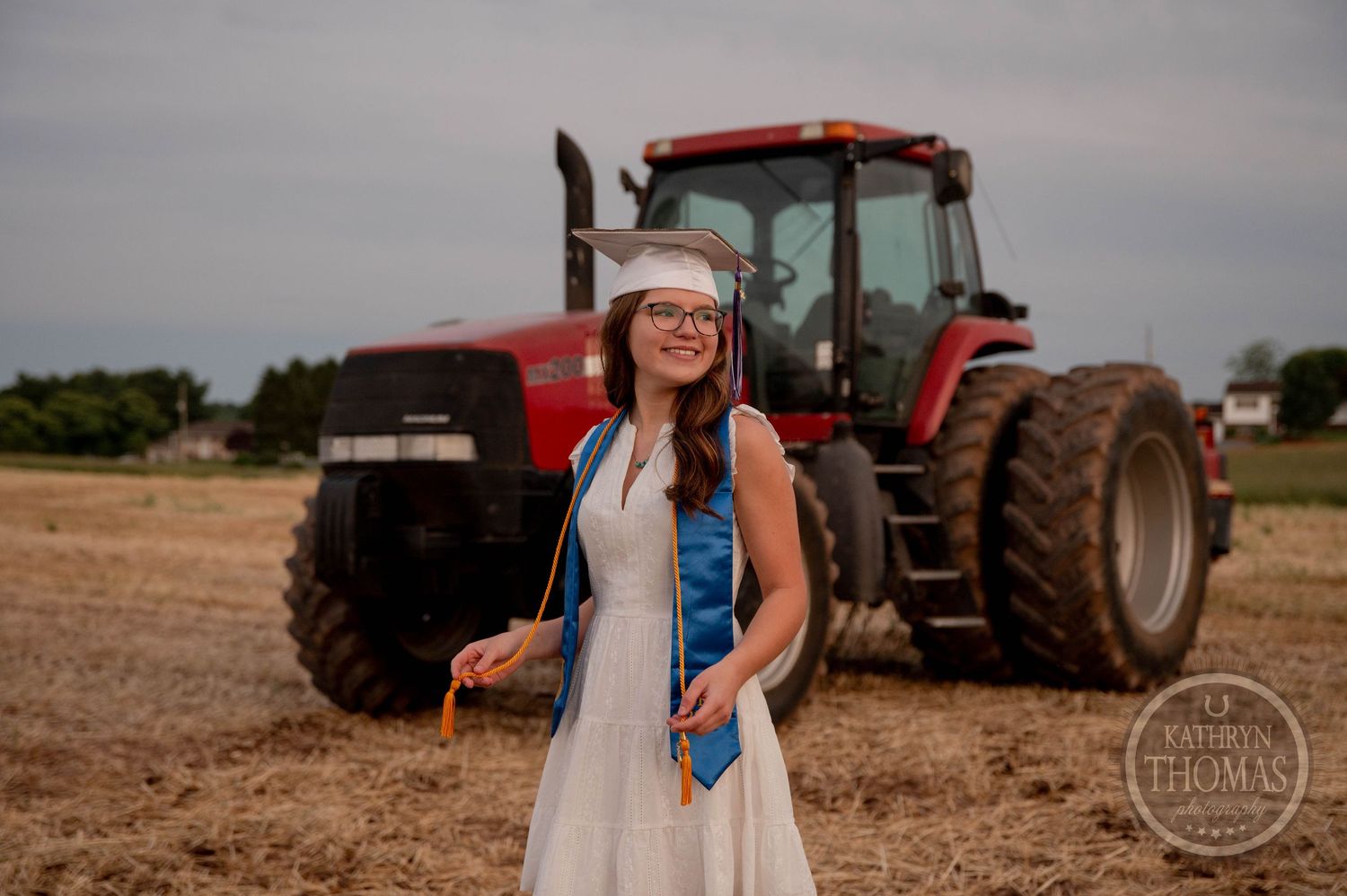 Country scene featuring a classic white dress outfit posed in front of a red Case IH tractor in a rural field setting.
