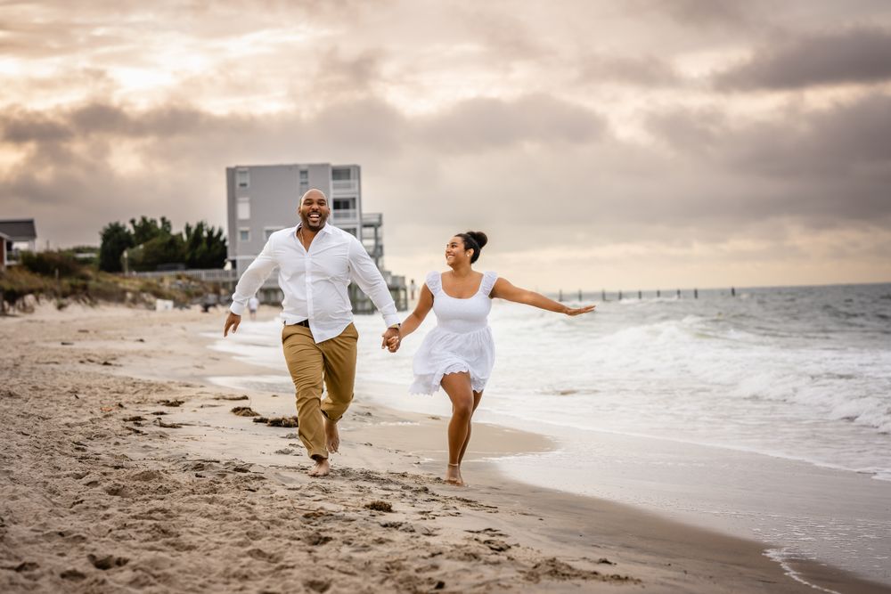 A joyful couple runs along the shoreline at sunset with waves crashing behind them.