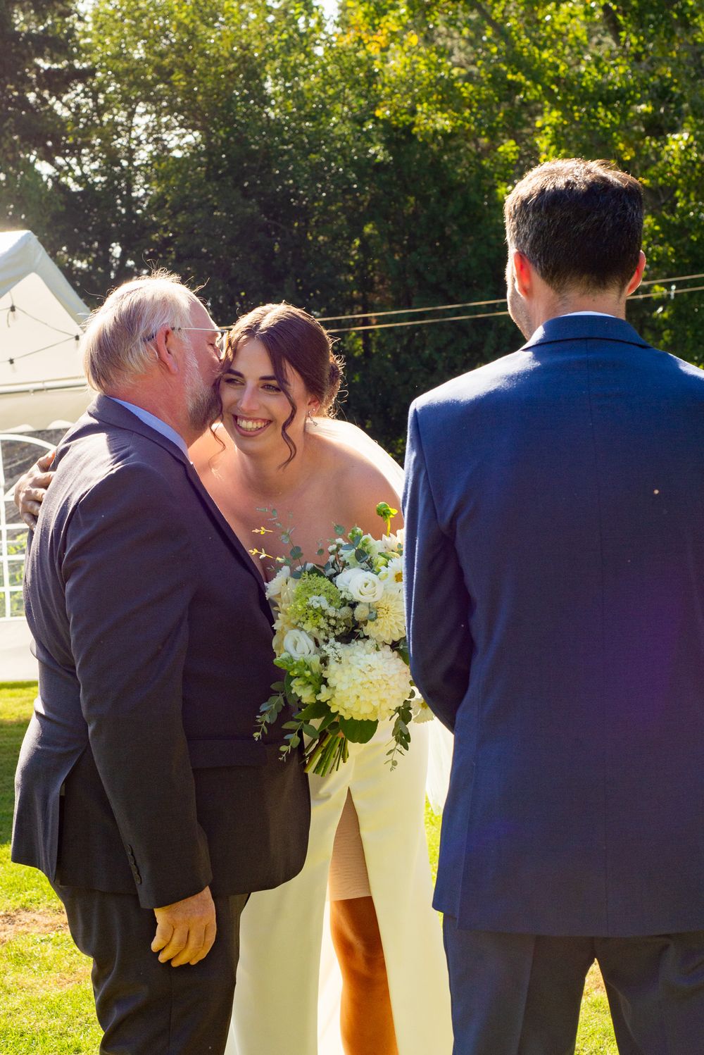 A joyful wedding celebration with guests and the bride outdoors on a sunny day.