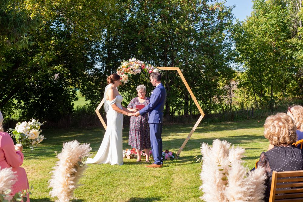 Wedding ceremony under a hexagonal arch decorated with flowers in a garden setting.