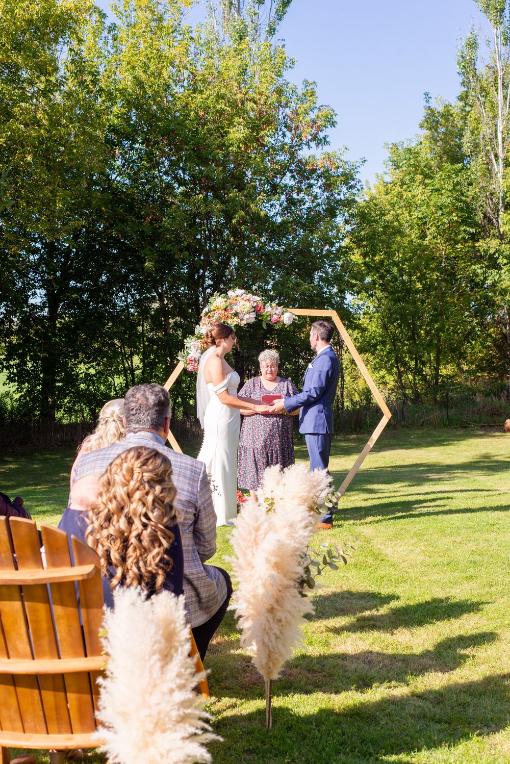 An outdoor wedding ceremony under a floral arch with pampas grass decorations.