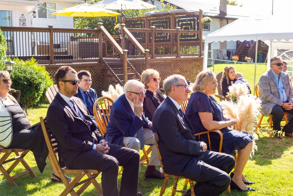 Wedding guests seated in wooden chairs outdoors during a garden ceremony.