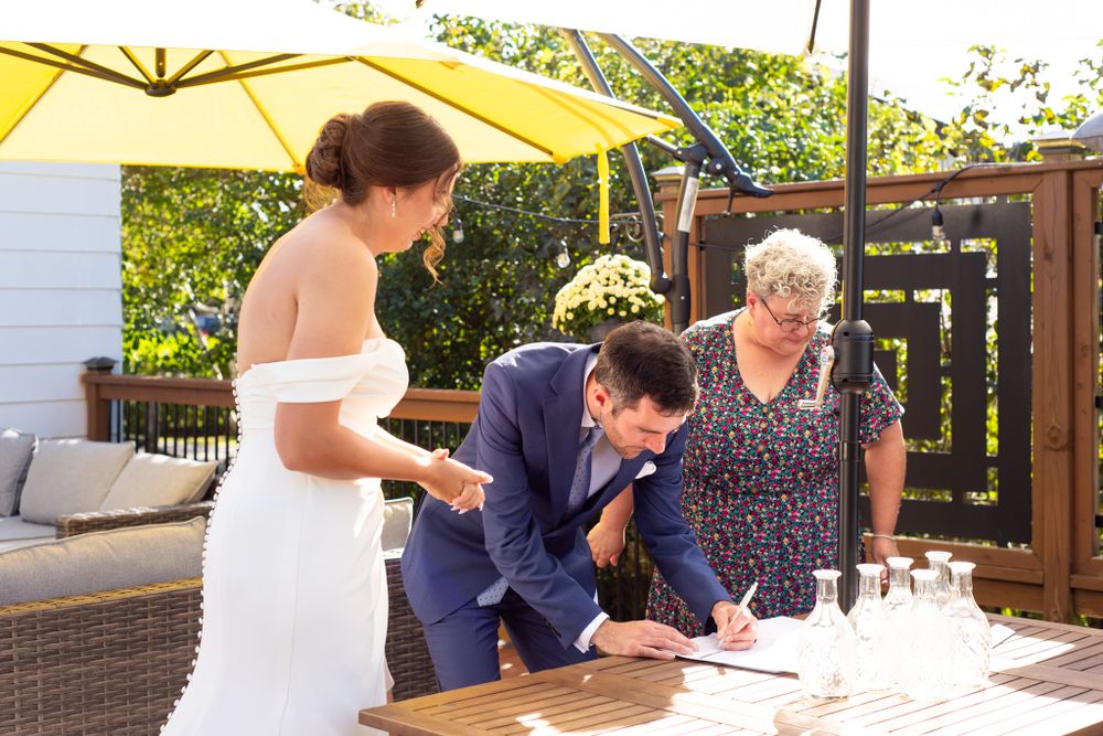 Wedding document signing ceremony taking place under yellow umbrella on outdoor patio.