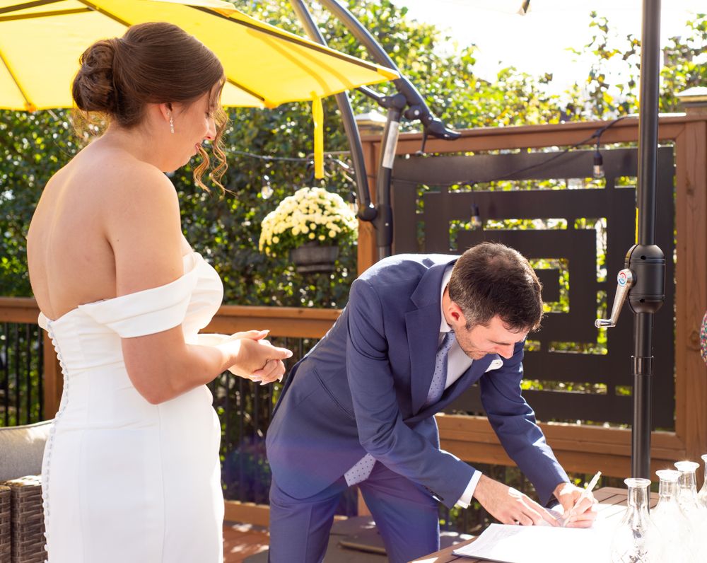 A couple signing their wedding documents under a yellow umbrella on an outdoor patio.