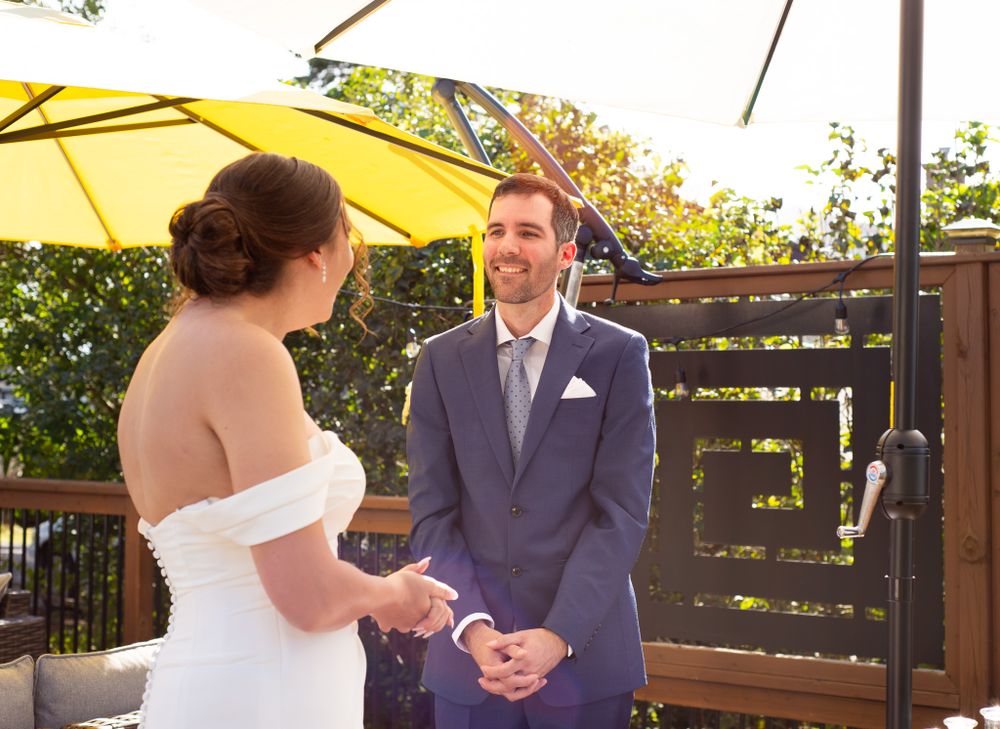 An outdoor wedding ceremony moment under a yellow umbrella on a wooden deck.