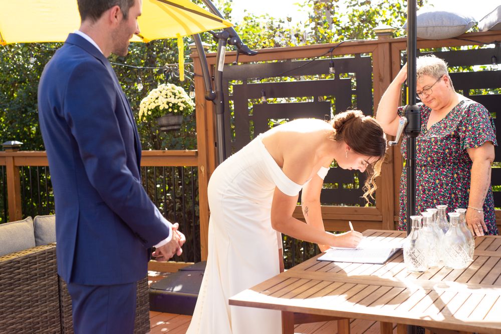 A wedding ceremony moment showing document signing at an outdoor venue with wooden decor.