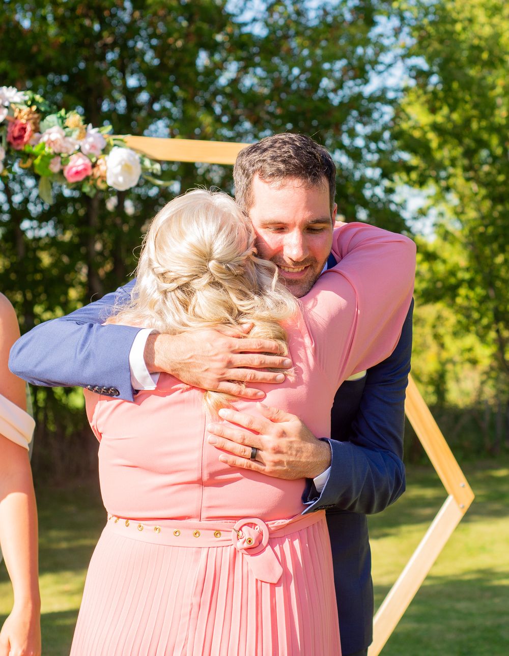 A warm embrace shared during an outdoor wedding ceremony with floral decorations.