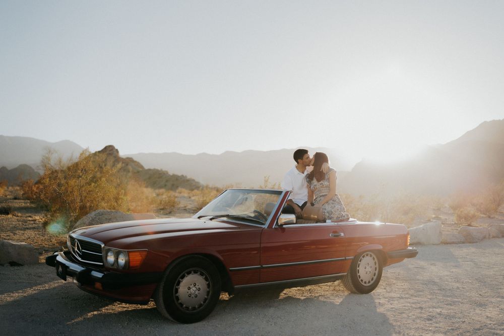 A classic red Mercedes convertible parked in a desert mountain landscape at sunset.