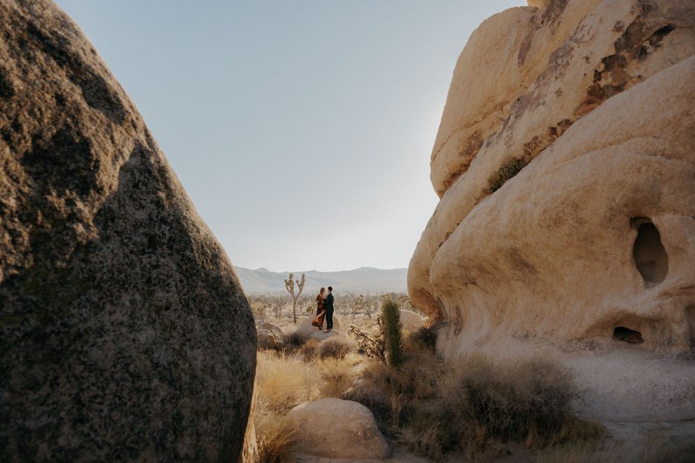 Hikers exploring rocky desert terrain surrounded by large sandstone formations on a hazy day.