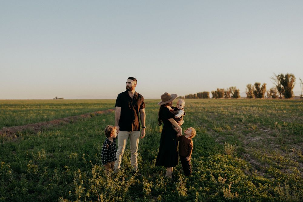 Two people stand in a grassy field at sunset with trees on the horizon during golden hour.